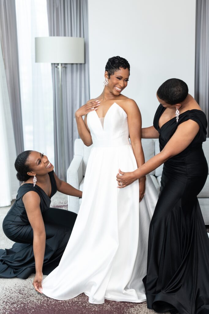 bride getting dressed with maid of honor and bridesmaid