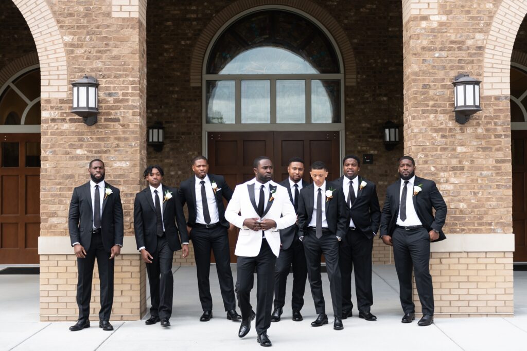 african american groom in white and black tuxedo with groomsmen in black tuxedos
